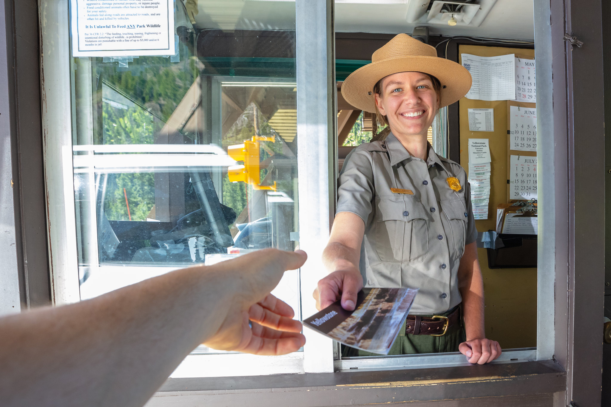 Woman in park ranger uniform handing brochure to driver in vehicle.