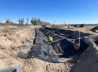 Three construction workers line a dirt trench with black tarp.