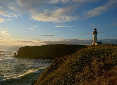 A white lighthouse stands against the ocean and cliffside.