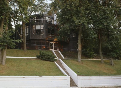 Circular dark brown home with steep, white steps and green lawn.