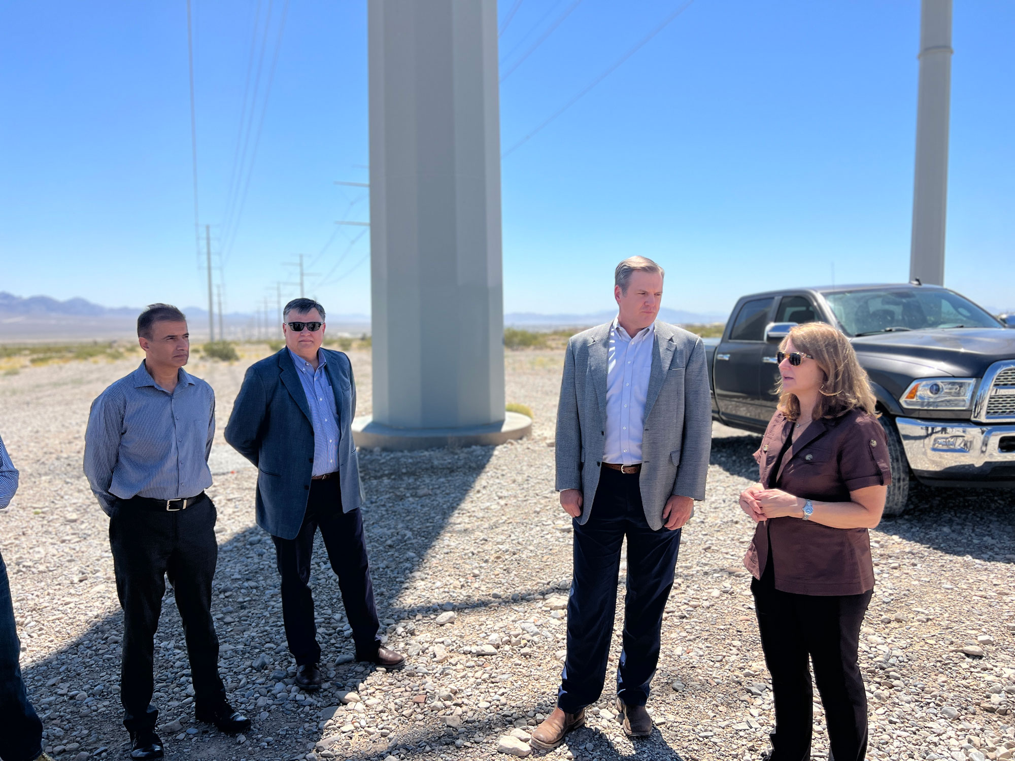 4 people talking to each other in front of truck and desert landscape 