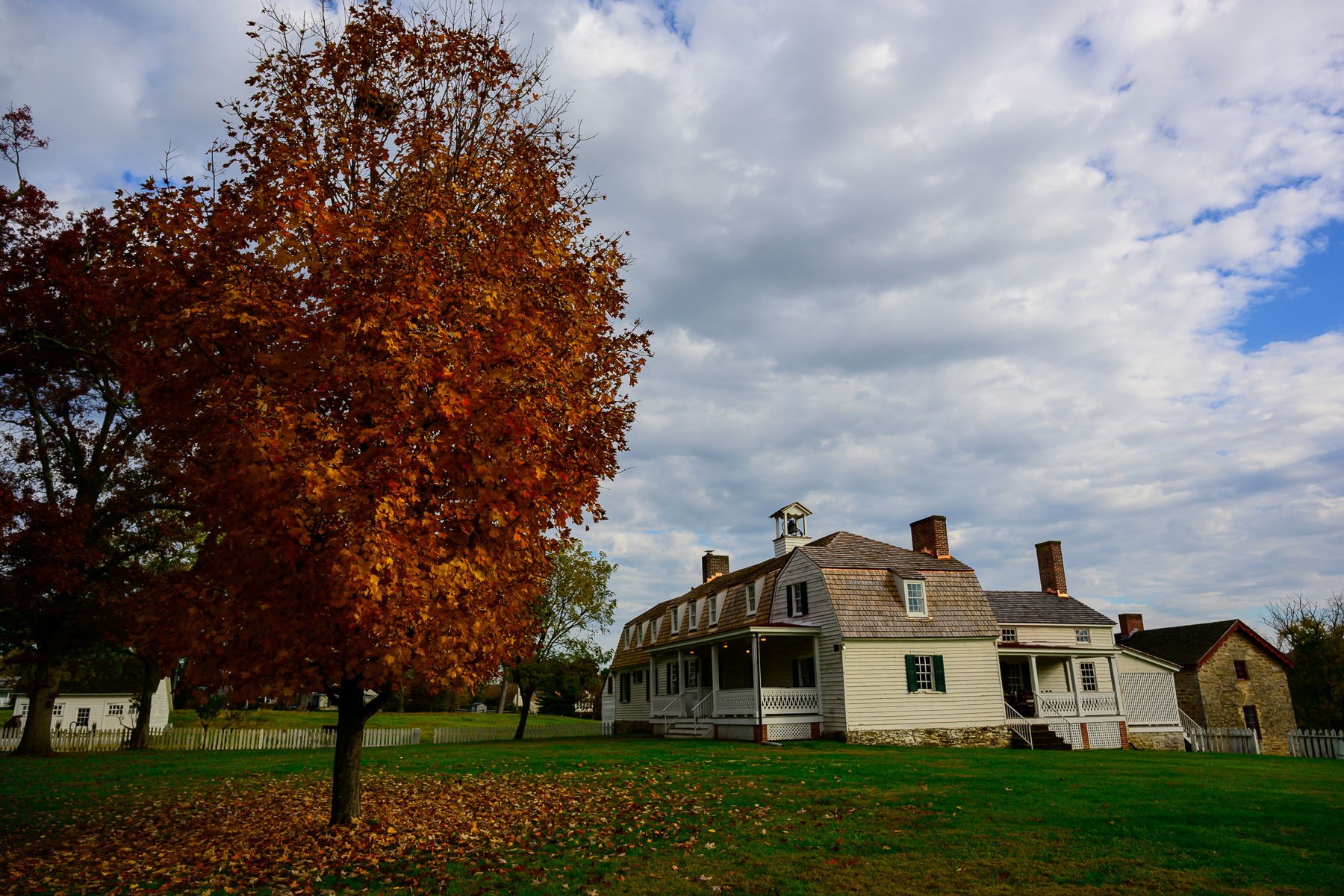 White building with shingle roof among fall colored trees.