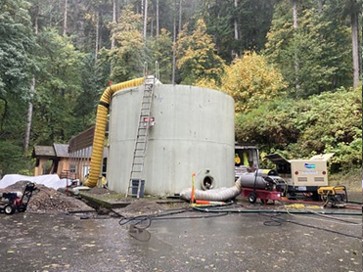  Gray drinking storage tank under construction with yellow and green trees in the background