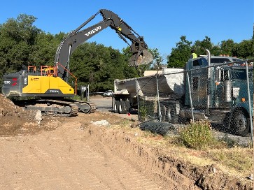 Yellow excavator moves dirt and stone into gray truck