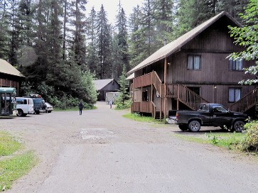  Brown housing units sit on either side of a paved parking lot with trees in the background