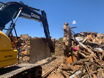 Yellow construction vehicle demolishes deteriorated, brick structure.