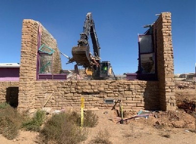 A yellow excavator demolishes a stone building.