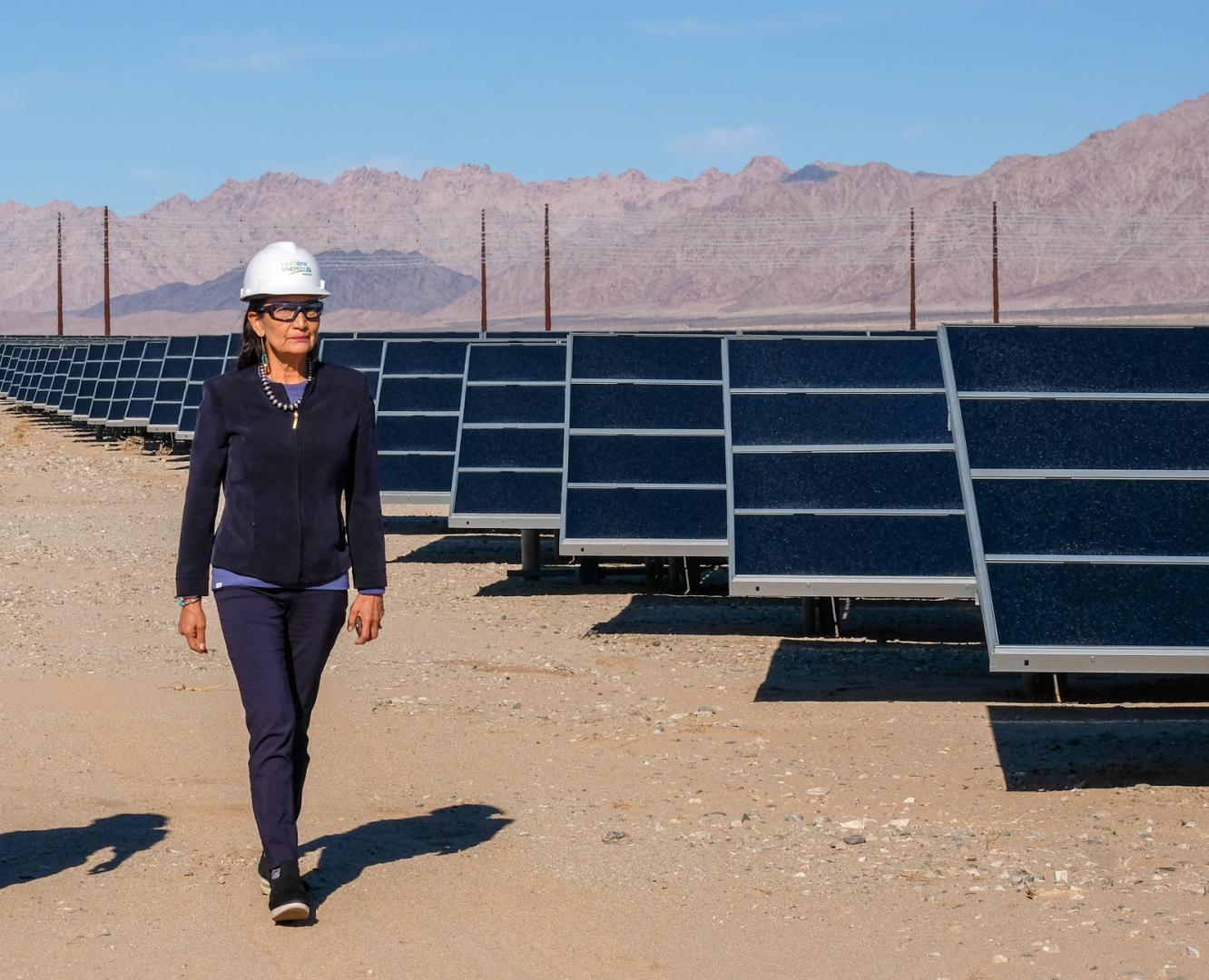 Secretary Haaland in hard hat walking next to solar panels. 