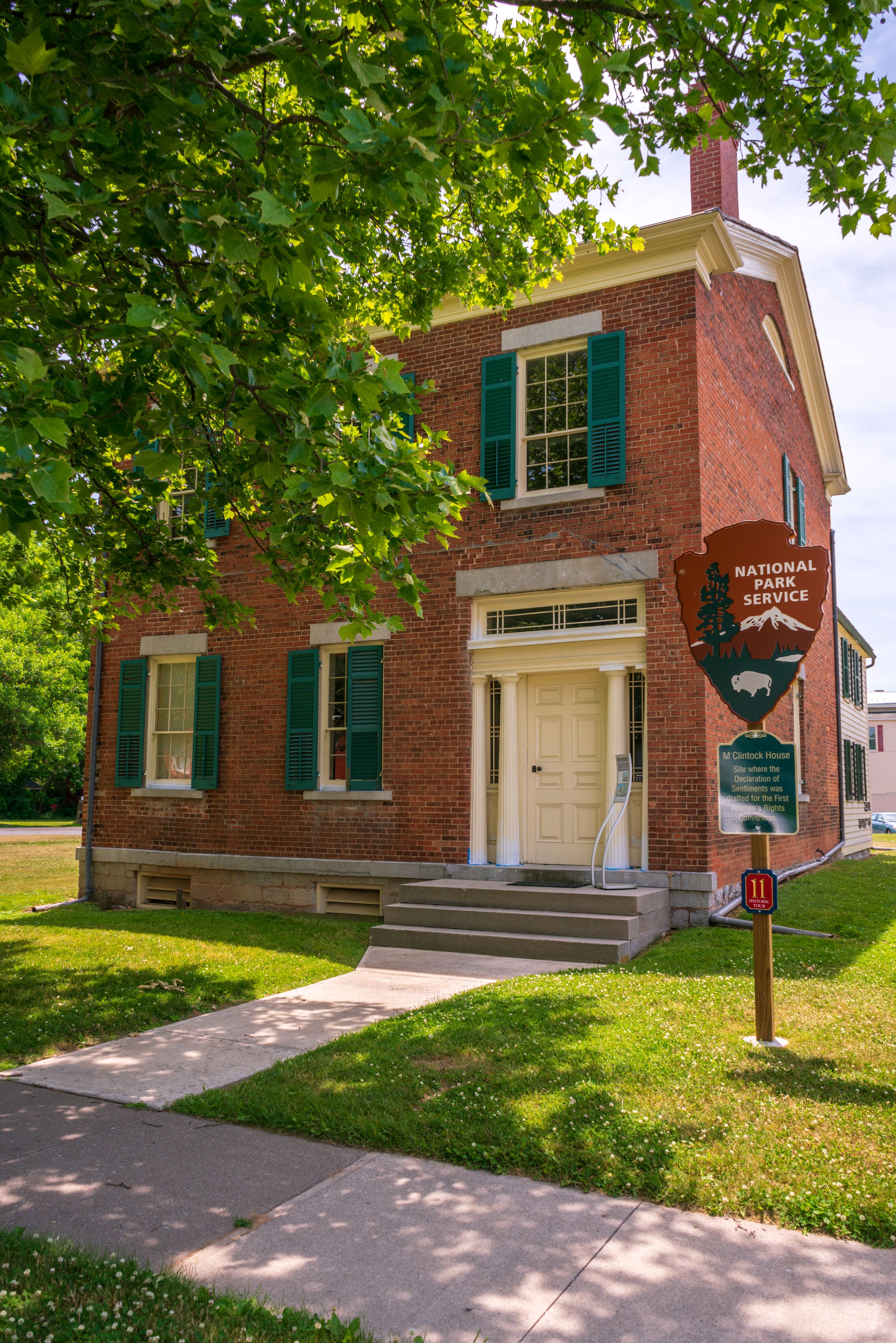 A two-story red brick building with green shutters and a white door.