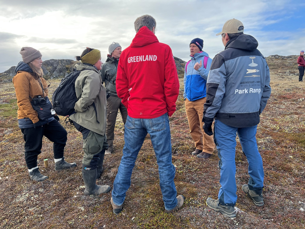 A group stands in a circle while someone speaks in Greenland