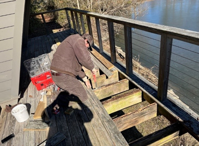 Man kneels on partially finished deck to install wooden boards.