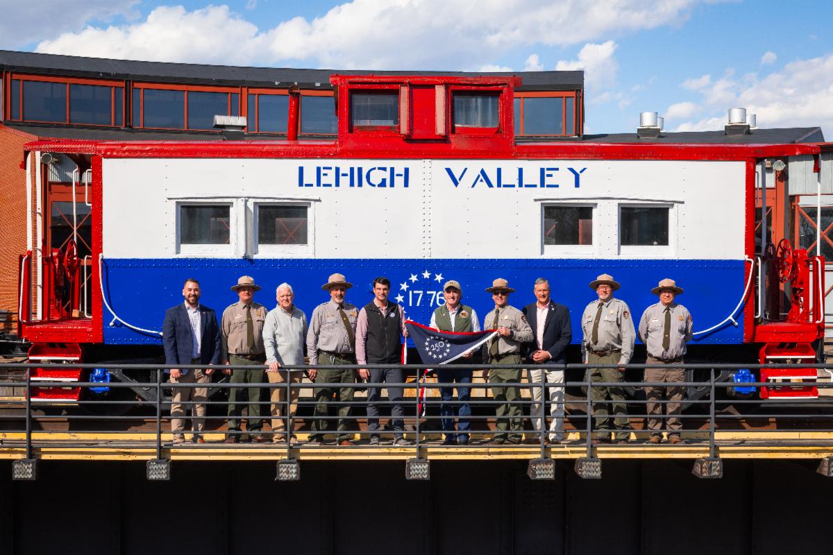 Park rangers holding 250 flag in front of steam engine train