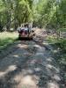 Construction vehicle sits on a dirt trail surrounded by grass and trees.