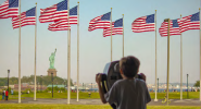 Child looking through binoculars at American Flags and the Statue of Liberty