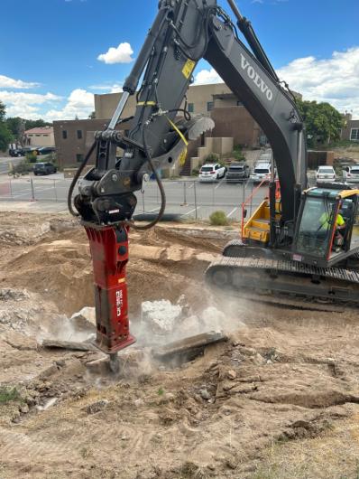Excavator jackhammer clearing and breaking down dirt and stone on school grounds.