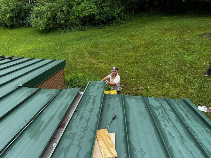 MAT member placing a metal roofing panel on a one-story quarters building.