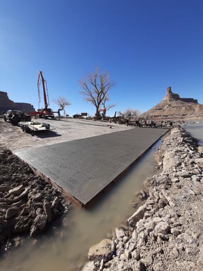 Construction vehicles sit on a concrete boat ramp surrounded by rocks.