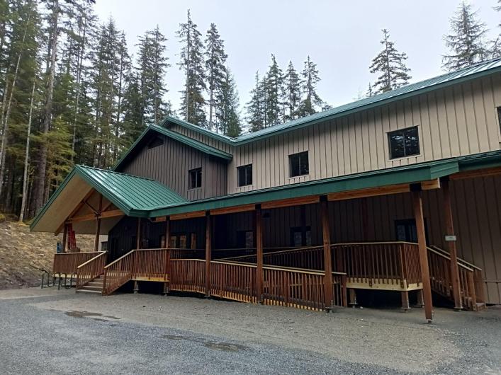 Two story housing building with tan siding and green roof.