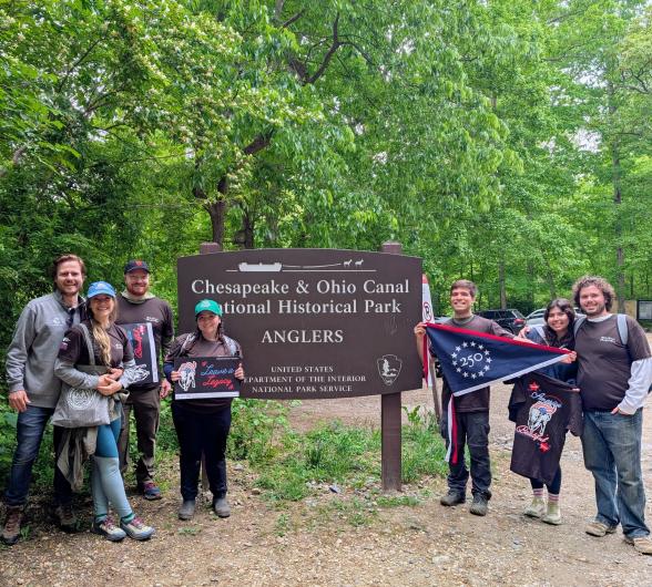 Group standing in front of trail sign with commemorative flag. 