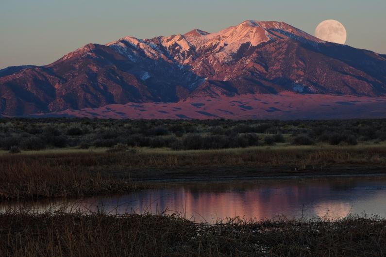 Supermoon behind sun-covered mountains at Great Sand Dunes National Park.