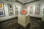 Exhibition gallery view with 14 framed serigraphs and vitrine filled with tools and materials explaining the silkscreen process.