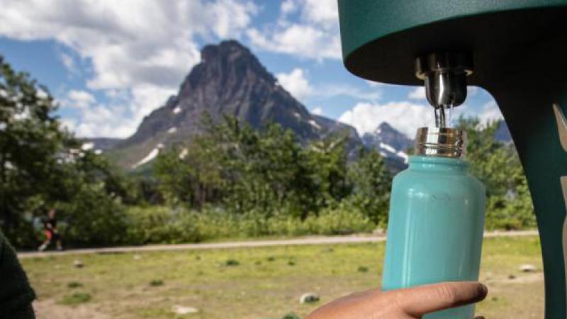 Arm with green sleeve filling up teal reusable water bottle at a water bottle filling station