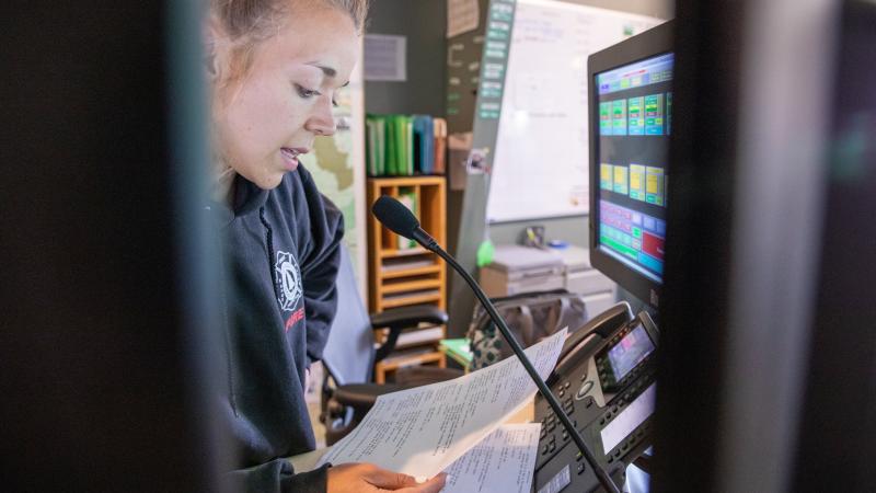 A dispatcher speaks into a microphone while sitting in front of a bank of computer monitors