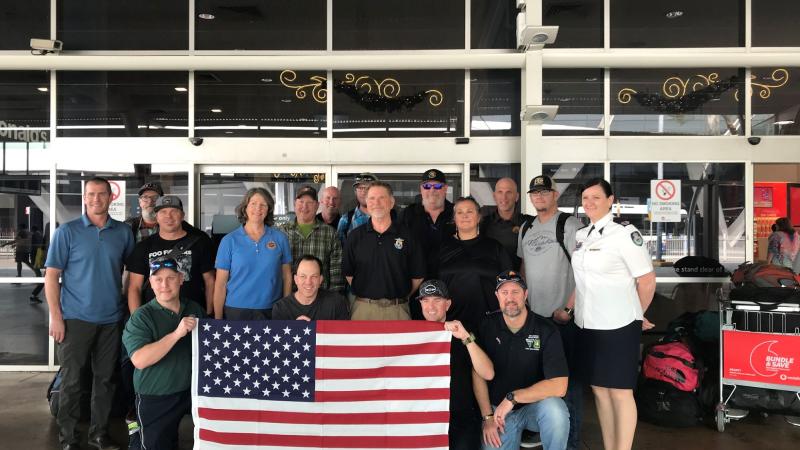 American firefighters arriving at airport in Sydney, Australia, holding a U.S. flag. 