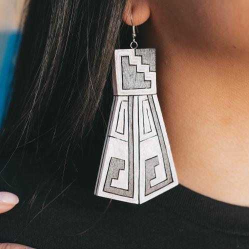Photograph of a wood carved earring hanging from a woman's ear.