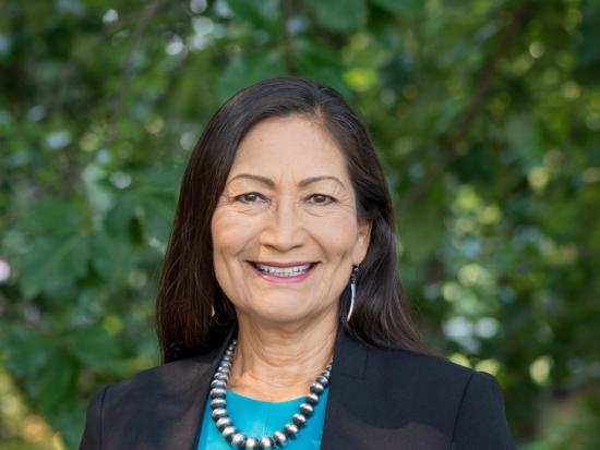 Secretary Deb Haaland smiling while wearing a black blazer and blue shirt