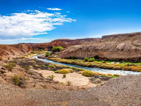 River valley surrounded by red cliffs and cloudy blue sky