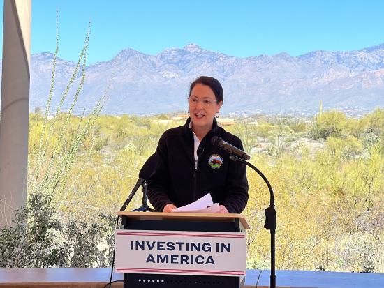Assistant Secretary Estenoz standing at Investing in America podeium in front of mountain landscape. 