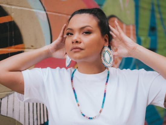 Photograph of woman wearing white and blue beaded earrings and a necklace. 