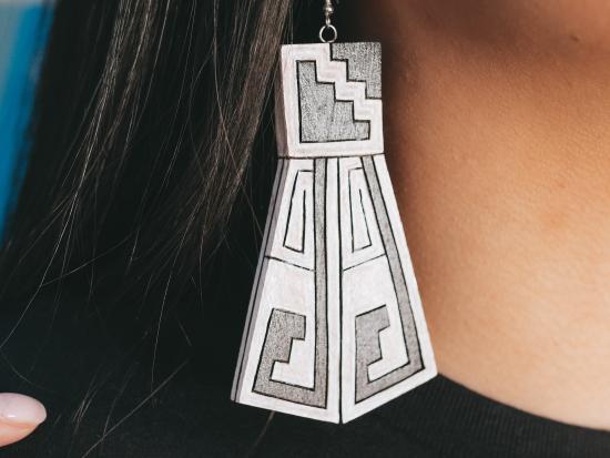 Photograph of a wood carved earring hanging from a woman's ear.