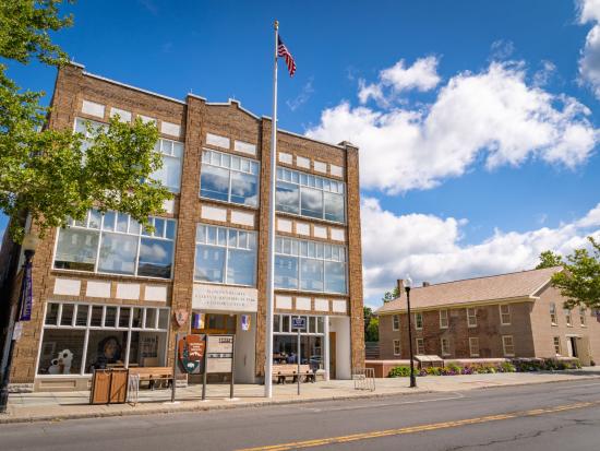 A three-story stone building with large glass windows and an American flag sits close to the road, and to its right, the brown brick Wesleyan Chapel is visible.