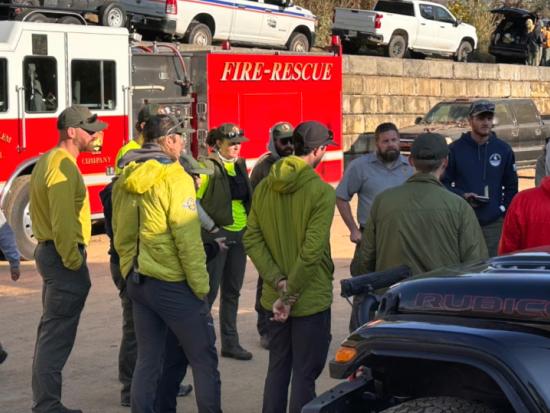 Wildland firefighters stand gathered in front of a red firetruck