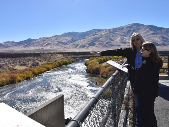 Two people standing on platform above river. Fall colors and mountains in the backdrop. 