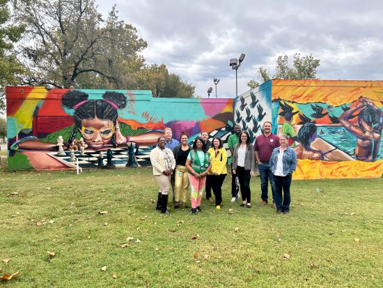 Group of people with Assistant Secretary Estenoz standing in front of mural. 