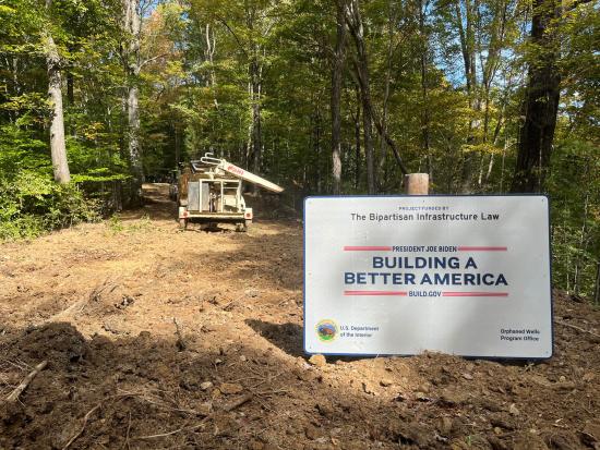 Dirt construction area in woods with large "Bipartisan Infrastructure Law" sign