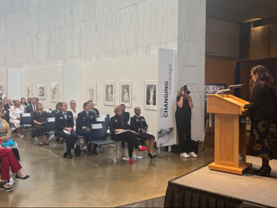 Secretary Haaland delivers remarks from a podium to seated audience members in a large, white marble foyer lined with portraits  