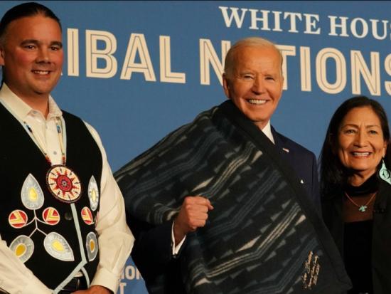 President Biden smiles with Secretary Haaland and Assistant Secretary Newland in front of a banner at the White House Tribal Nations Summit