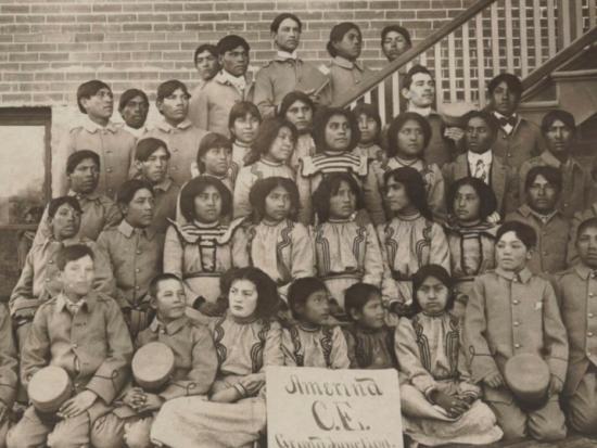 Historic image of children gathered by a stairwell posing for a photo at a federal Indian boarding school