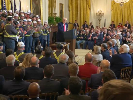 President Trump standing in front of podium applauding a group of coal miners in safety gear