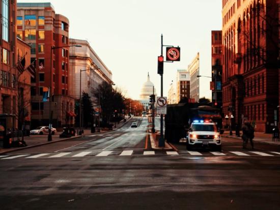 A police vehicle with red and blue lights is seen from a street in downtown Washington, D.C. with the Capitol building dome in the distance