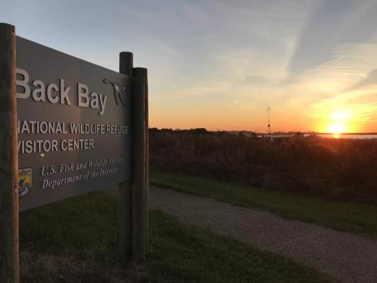 Back Bay National Wildlife Refuge entrance sign with a sunset in the background.