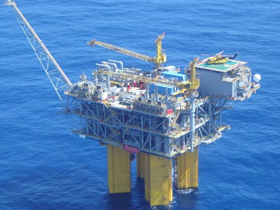 A yellow and gray oil rig stands in the ocean 