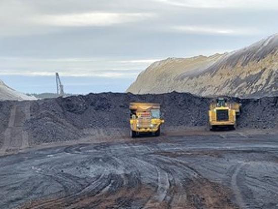 Two yellow mining operation trucks on dark soil.
