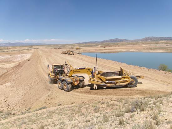 Construction vehicles sit on the dirt perimeter of large body of water.