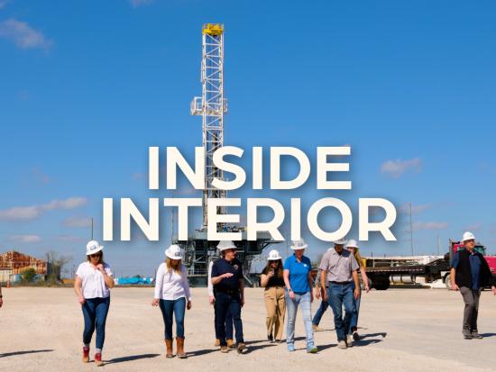 People walk across a wide oil field dirlling site 