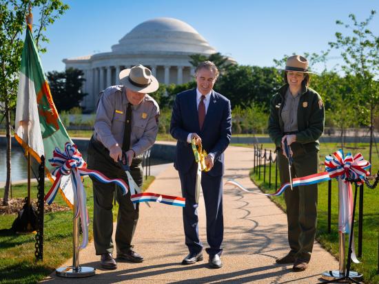 Secretary Burgum and 2 park rangers holding giant scissors at a ceremonial ribbon cutting.